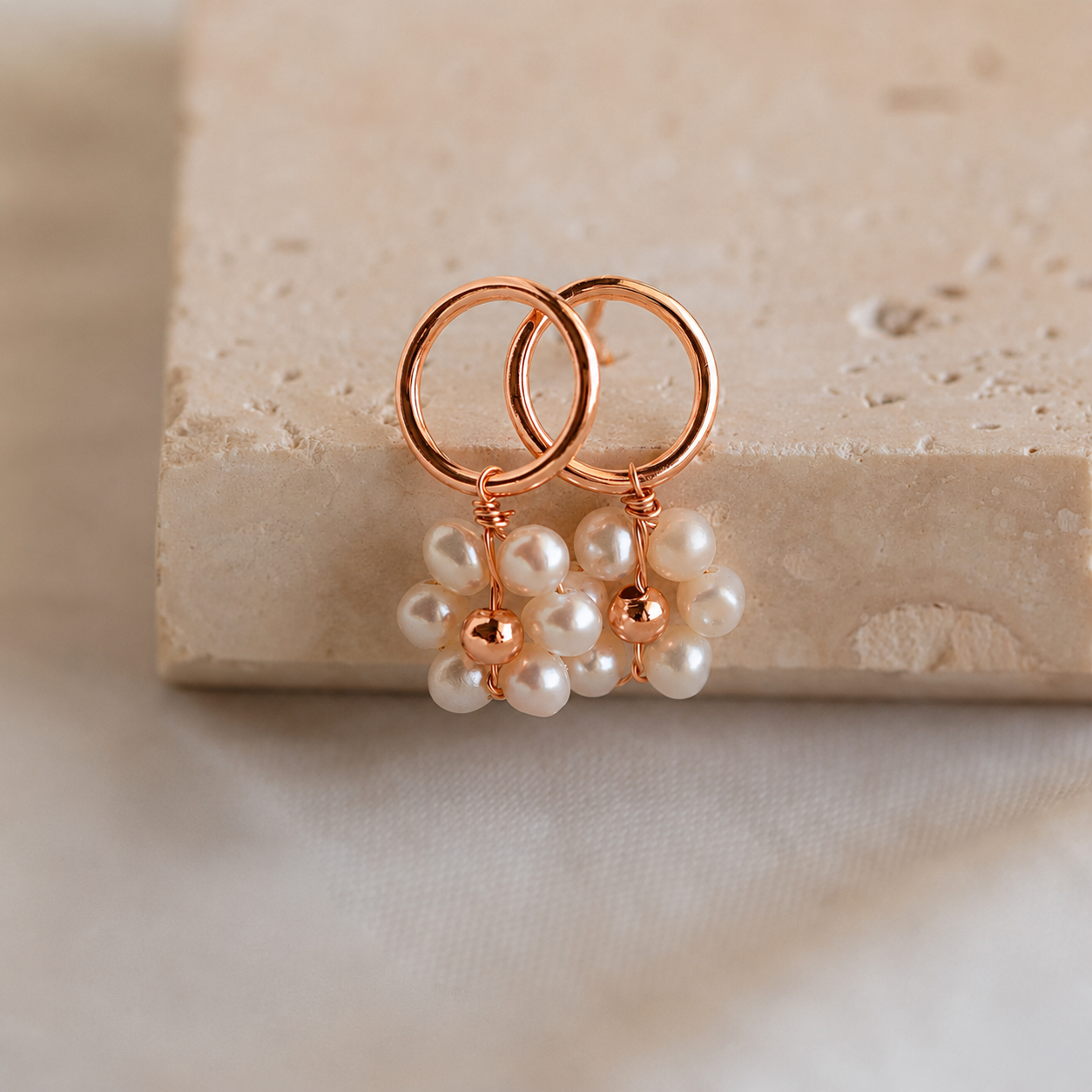 Rose gold earrings with pearl-like beads on a beige stone surface